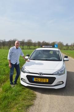 Ruud Monsuwé bij de voorkant van de lesauto